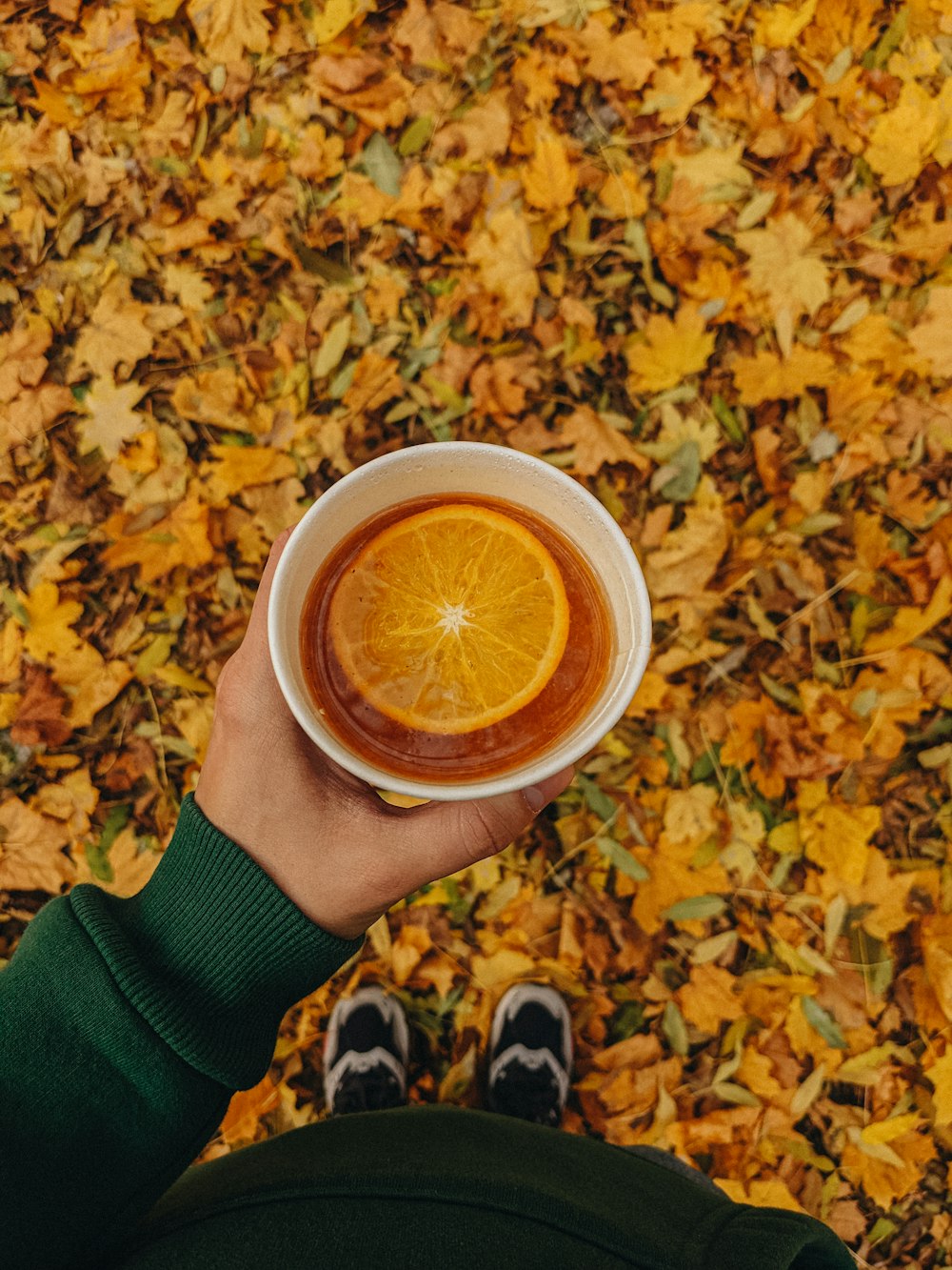 a person holding a cup of tea with an orange slice in it