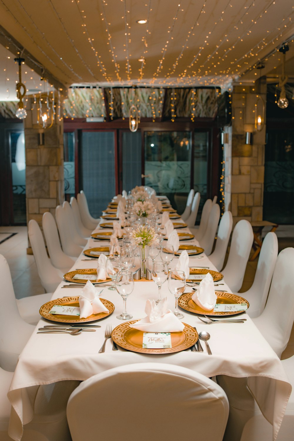 una mesa larga con sillas blancas y platos dorados