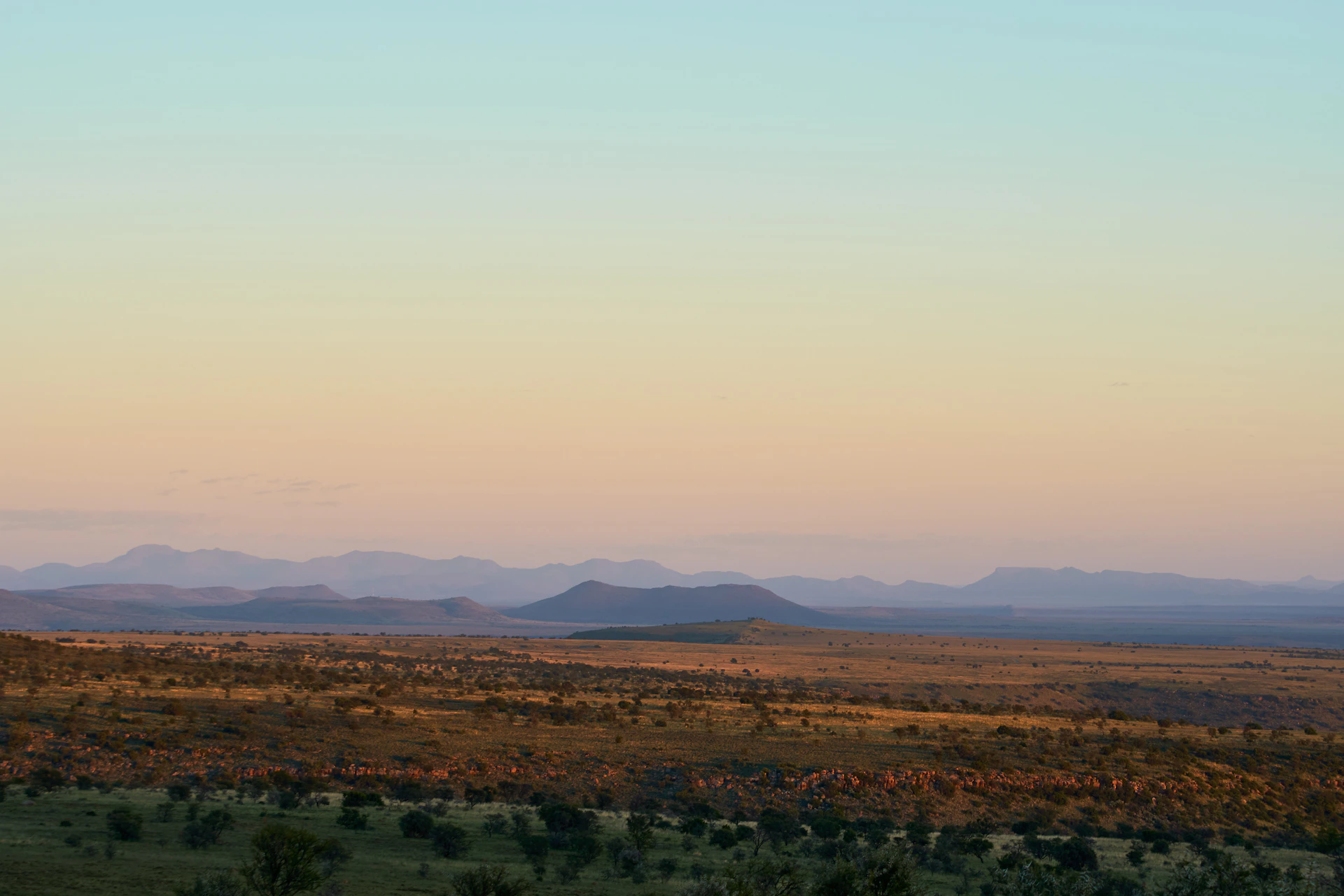 Wide open plains with riders silhouetted against a vibrant sunset sky.