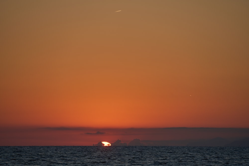 the sun is setting over the ocean with a sailboat in the foreground