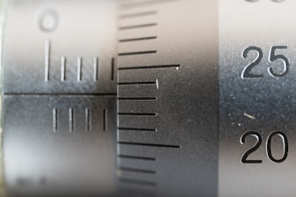 Close-up view of a metal scale or measuring instrument with engraved numbers and lines, ranging from 20 to 25. The surface appears metallic with a brushed texture, suggesting a precision tool likely used for measurement.