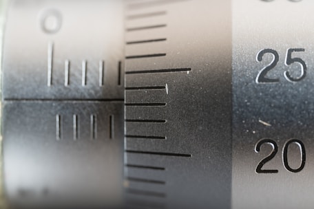 Close-up view of a metal scale or measuring instrument with engraved numbers and lines, ranging from 20 to 25. The surface appears metallic with a brushed texture, suggesting a precision tool likely used for measurement.