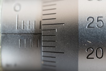 Close-up view of a metal scale or measuring instrument with engraved numbers and lines, ranging from 20 to 25. The surface appears metallic with a brushed texture, suggesting a precision tool likely used for measurement.
