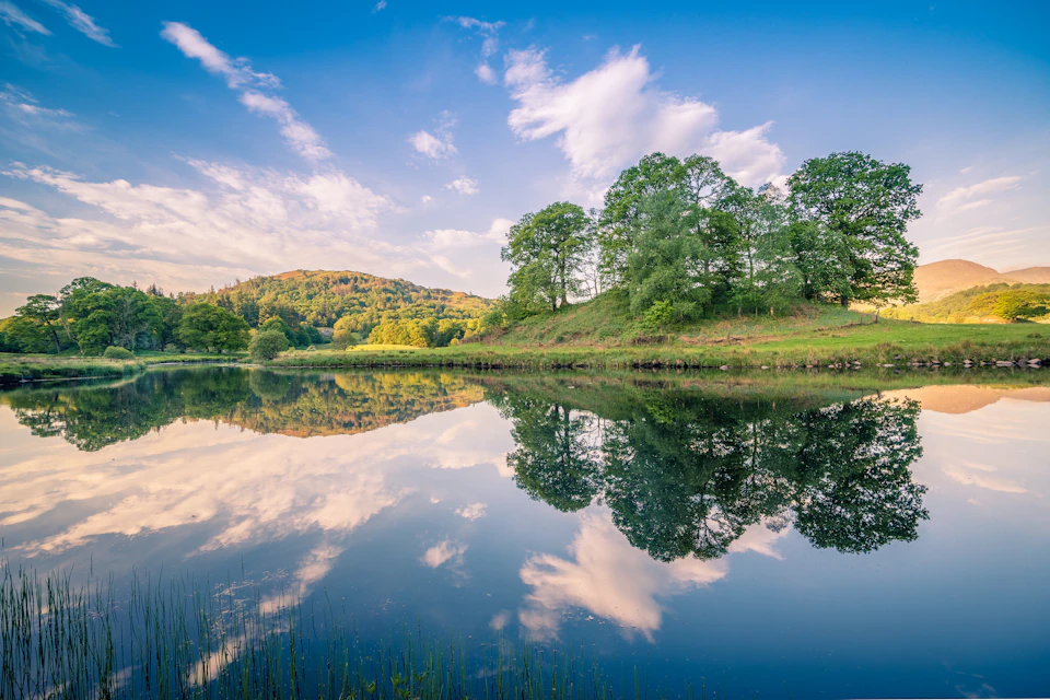 Serene lake surrounded by lush green trees and rolling hills with clear blue sky above
