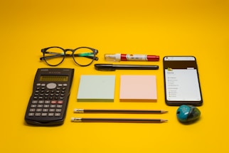 a calculator, pen, eyeglasses, notepad, pencils