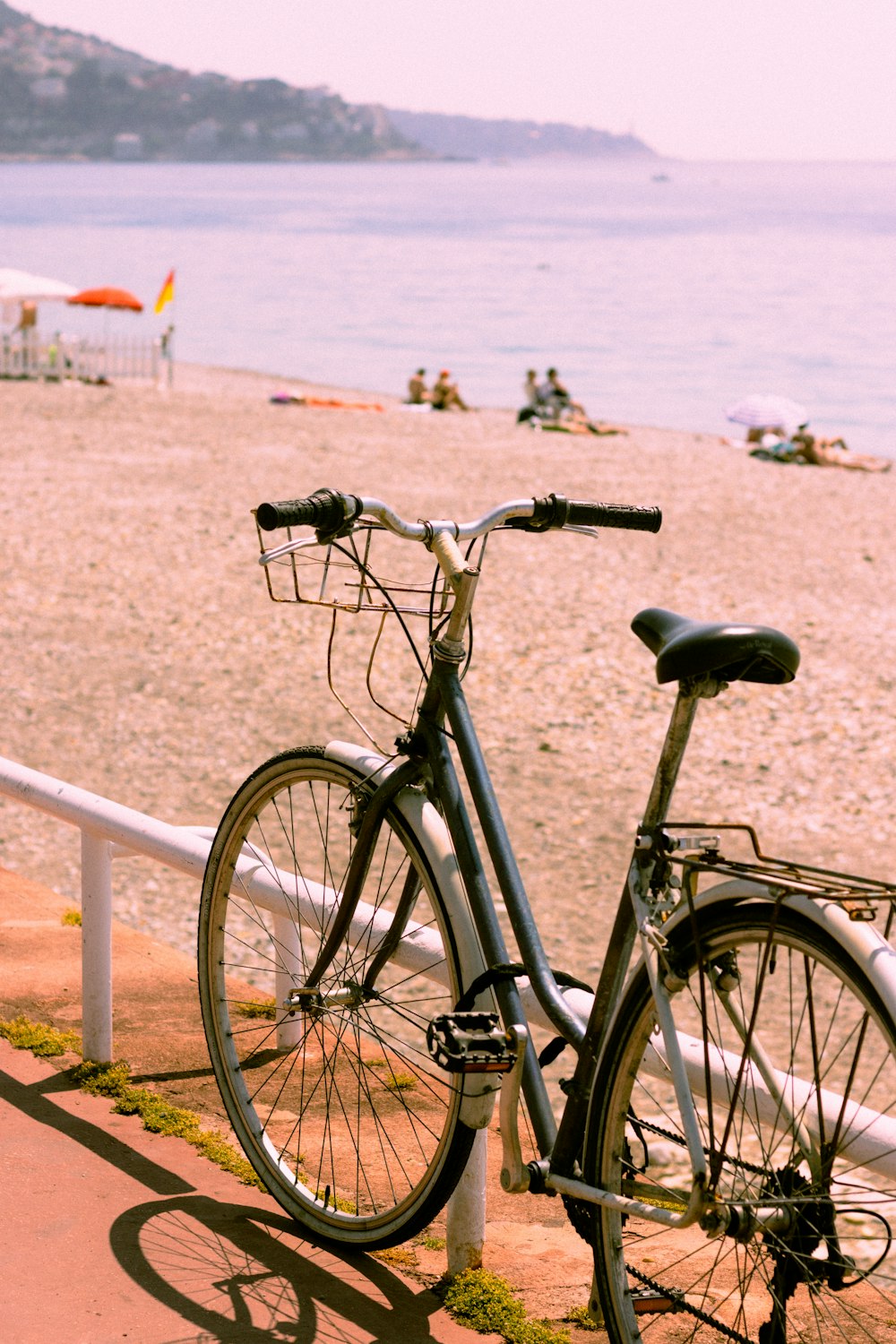 a bicycle parked on the beach next to a railing