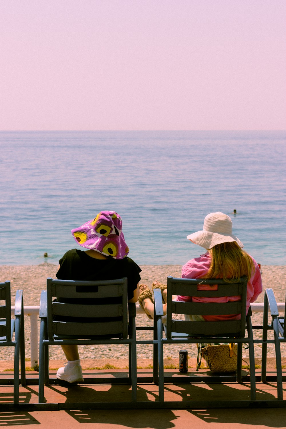 two women sitting on chairs facing the ocean