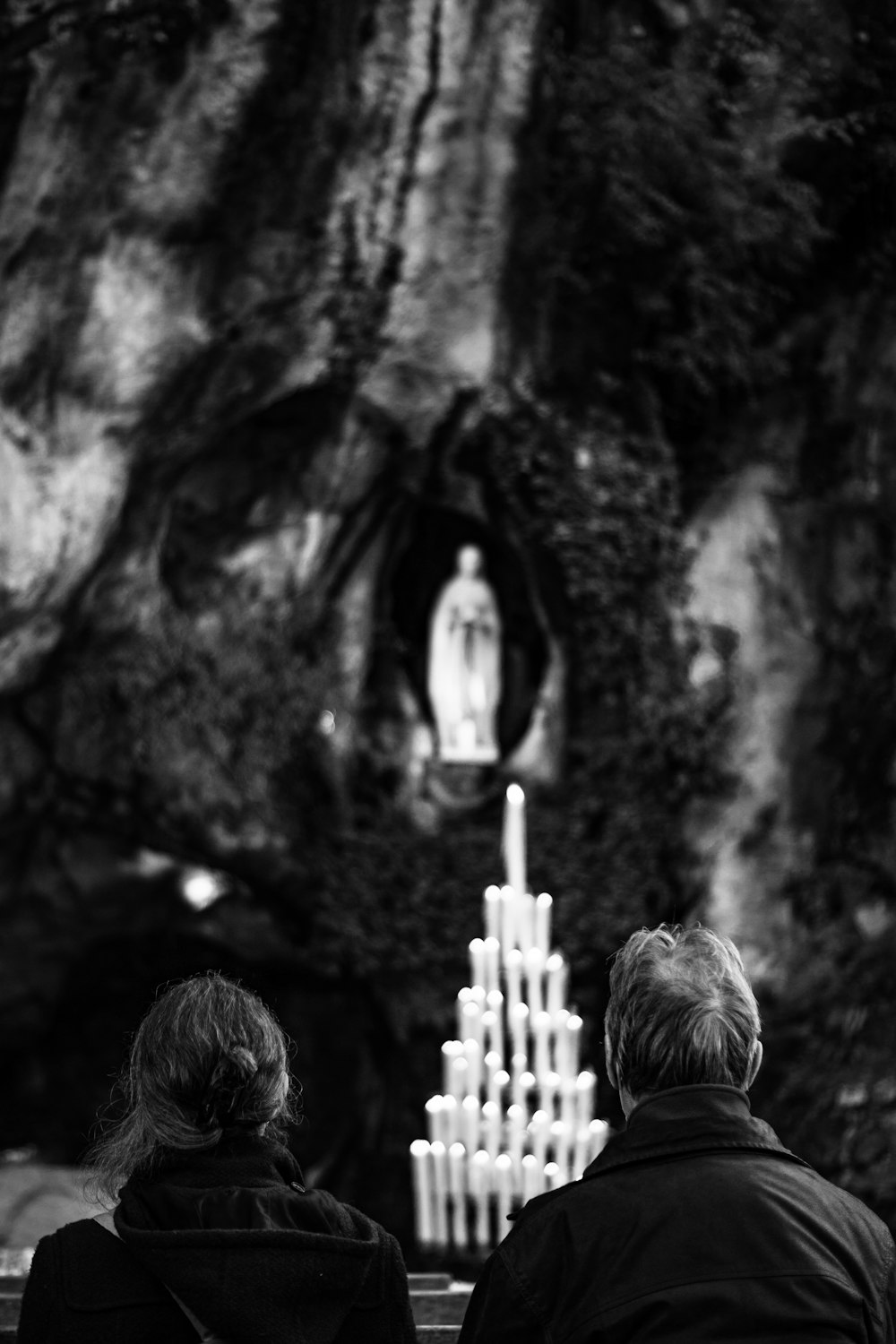 two people sitting on a bench looking at a statue