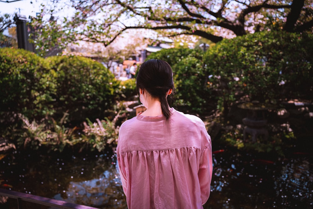 분홍색 셔츠를 입은 여자가 연못을 바라보고 있다