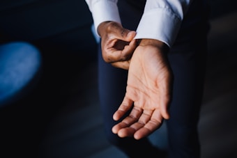 A person adjusting the cuff of a white sleeve, focusing on the hand and forearm. The image highlights the skin tone contrast between the hand and the fabric. Gentle light creates a soft shadow on the surrounding area.