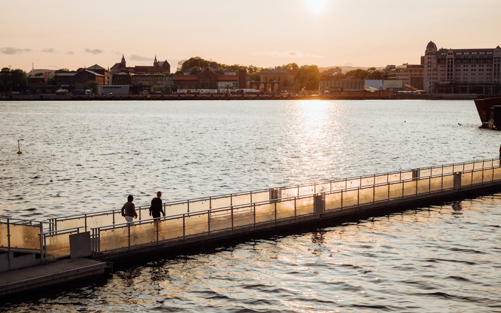 a couple of people walking across a bridge over a body of water