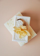 Close-up of a delicate heart-shaped soap resting on soft purple silk with grape clusters beside it.