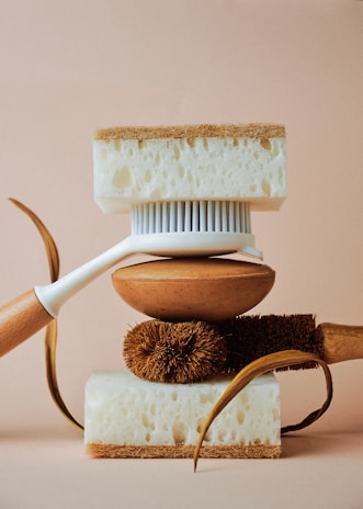 A balanced arrangement of cleaning tools including a white-handled brush, natural fibers, and two thick sponges with contrasting textures.
