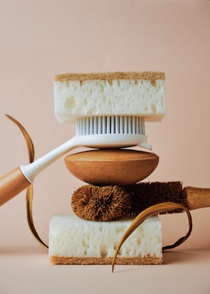 A balanced arrangement of cleaning tools including a white-handled brush, natural fibers, and two thick sponges with contrasting textures.