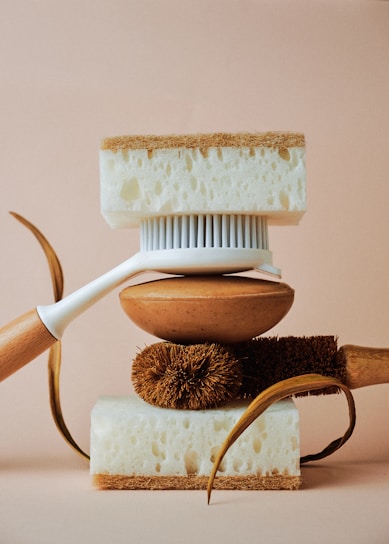 A balanced arrangement of cleaning tools including a white-handled brush, natural fibers, and two thick sponges with contrasting textures.
