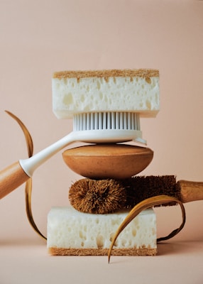 A balanced arrangement of cleaning tools including a white-handled brush, natural fibers, and two thick sponges with contrasting textures.