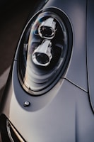 A close-up of a sleek car headlight with a modern and aerodynamic design, featuring intricate details and reflective surfaces. The lighting highlights the smooth contours and craftsmanship.