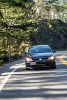 A sleek Volkswagen Golf cruising along a coastal highway with waves crashing nearby.