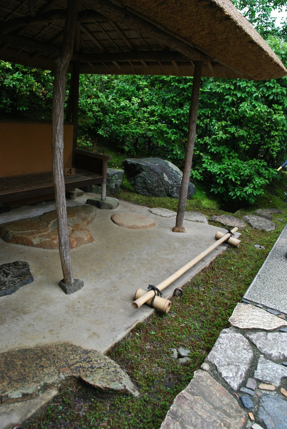 a wooden bench sitting under a shelter next to a forest