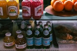 A display shelf featuring bottles of various drinks such as juices and sparkling water. Bundaberg bottles are at the top with flavors like tropical mango and pink grapefruit. Next to them are fresh oranges on a platter. Below, Pellegrino sparkling water bottles and small round bottles of Martinelli's apple juice are arranged. To the right, several croissants rest on a lined tray.
