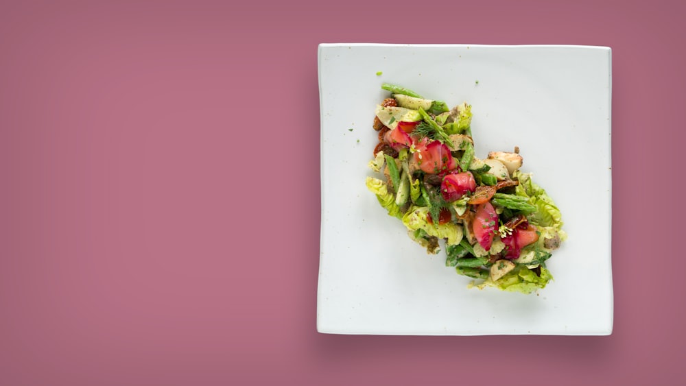 a white plate topped with a salad on top of a pink table