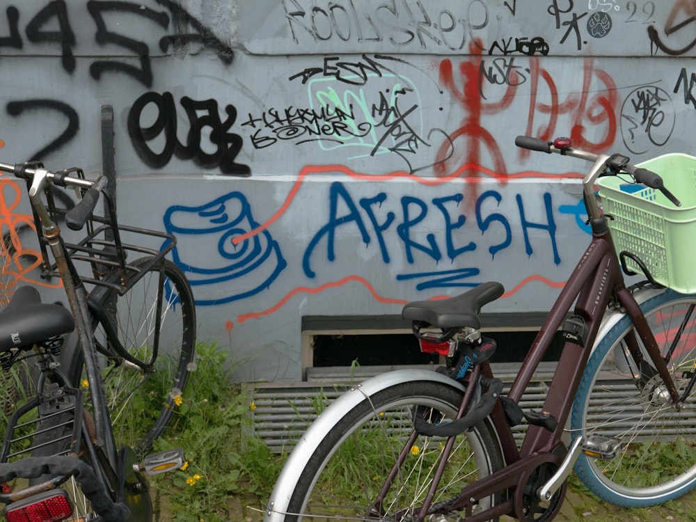 two bikes parked next to each other in front of a wall with graffiti