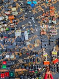A variety of electrical components are arranged neatly on a dark surface. The components include switches, plugs, connectors, and other hardware, each displaying different colors and forms. The words on the surface, partially visible, seem to be part of a packaging or material brand. An array of colors, shapes, and metal finishes make up the intricate display.