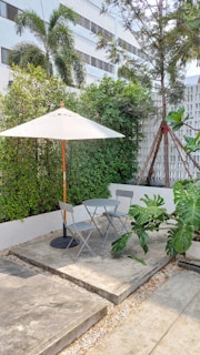 A cozy outdoor patio scene featuring a sleek aluminum frame sofa set and a round rattan dining table under a large, sturdy umbrella.