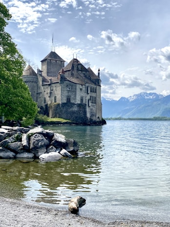 The iconic medieval castle of Chillon on the shores of Lake Geneva surrounded by calm water and lush greenery.