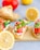 Slices of toasted bread topped with creamy spread and garnished with fresh vegetables like tomatoes, cucumbers, and parsley. A lemon and tomato are in the background, adding vibrant color to the composition.