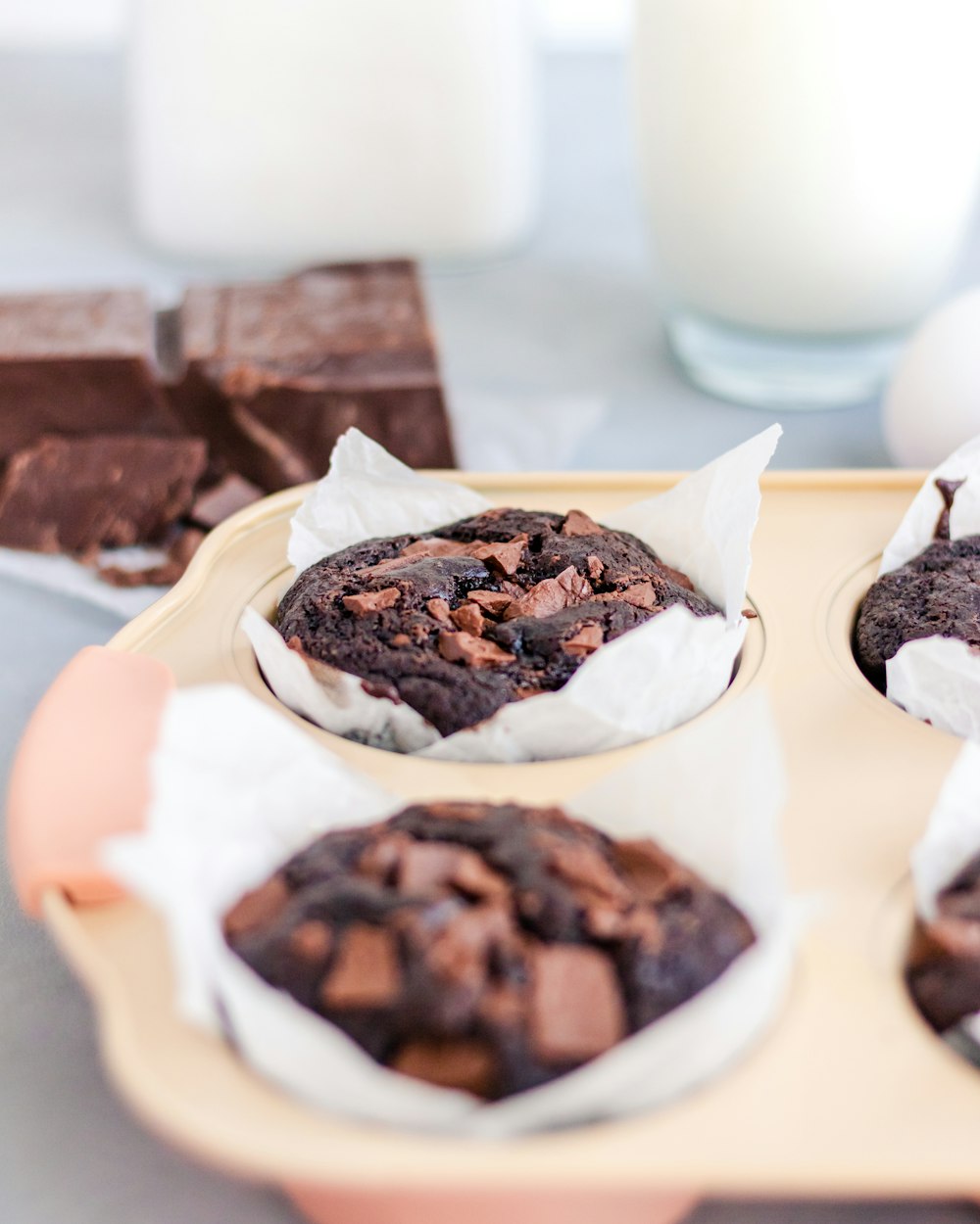 a tray of chocolate muffins next to a glass of milk