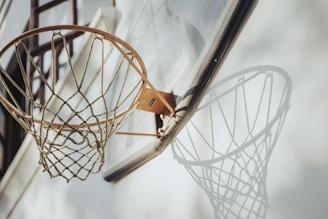 A white durable basketball net hanging on an indoor court hoop, perfectly framed by polished wooden floors.