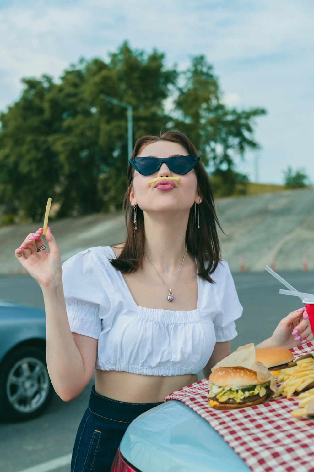 Una mujer en un crop top sosteniendo un cigarrillo y un sándwich