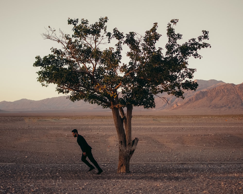 a man walking past a tree in the middle of a desert