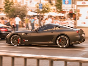 A sleek matte black sports car with red accents roaring down an urban street at dusk