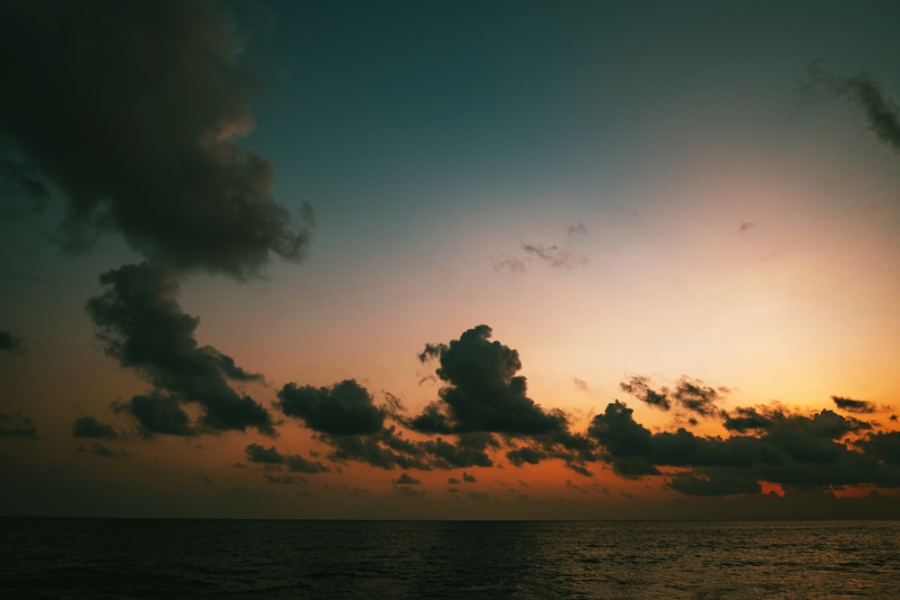 the sun is setting over the ocean with clouds