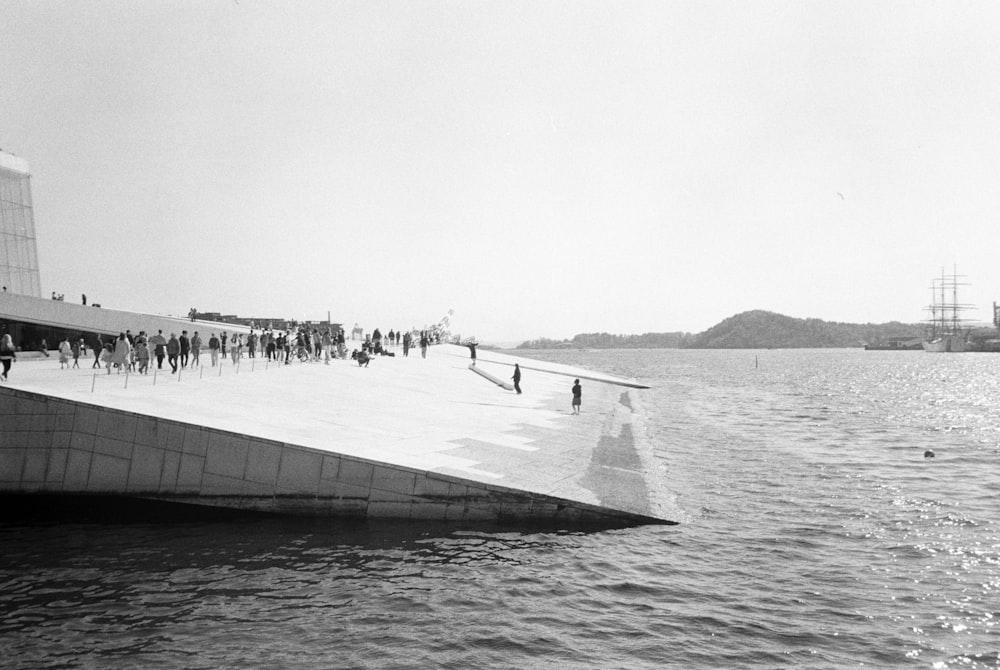 a black and white photo of people walking on a pier
