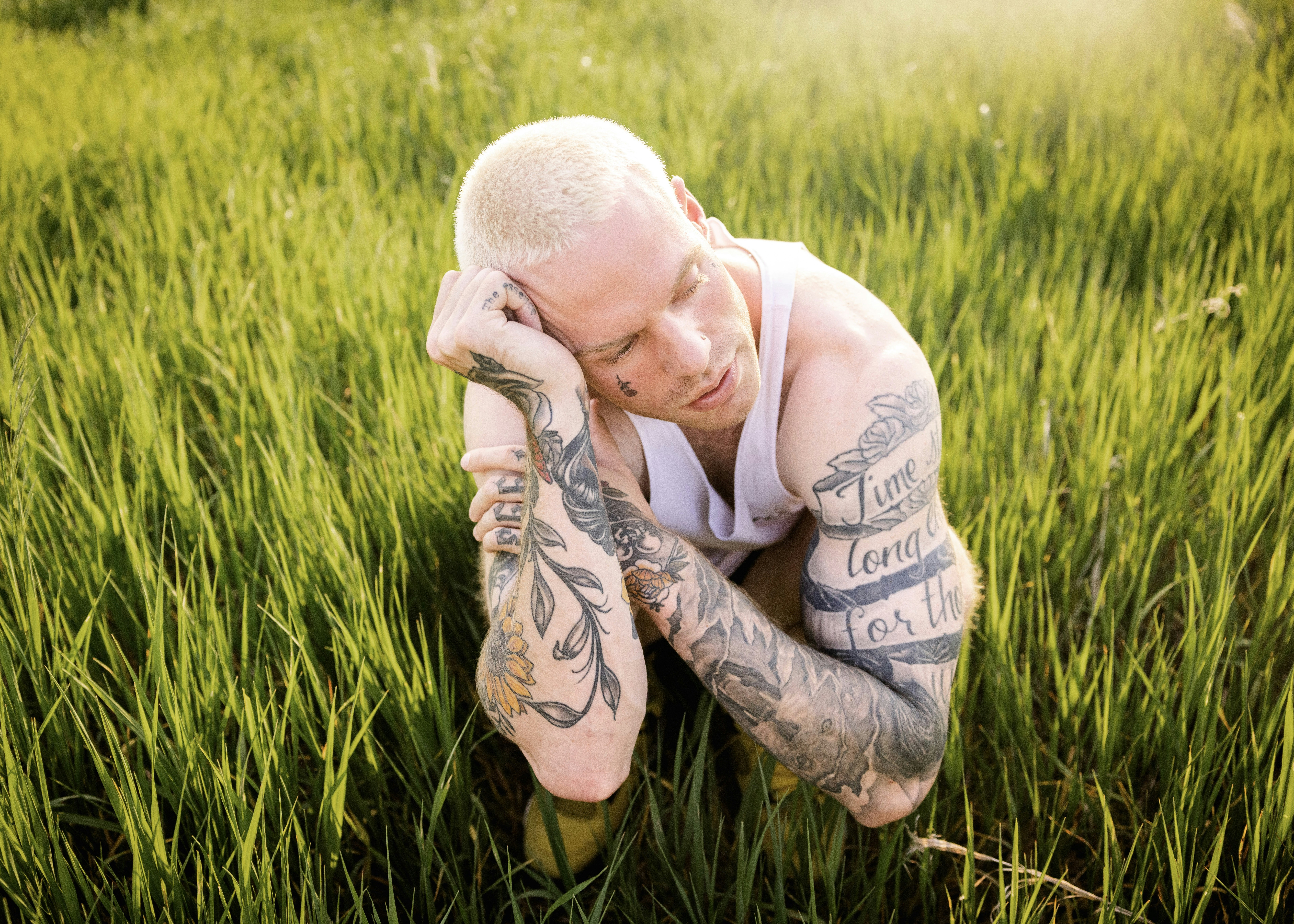 a tattooed man sitting in a field of tall grass