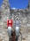 Two electric vehicle charging stations with signs attached to a stone wall. One sign reads 'Tesla Vehicle Charging' and the other reads 'Electric Vehicle Charging.' The background features a rustic, weathered stone wall beneath a clear blue sky.