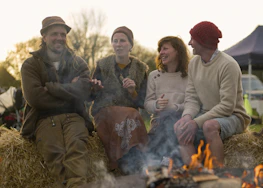 A group of friends laughing and sharing stories around a campfire at a bluegrass festival.