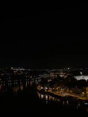 Nighttime cityscape featuring illuminated buildings and a calm river reflecting lights.