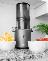 A bright, modern kitchen setting with various cold pressed juice bottles and fresh ingredients on the counter.