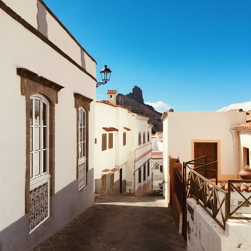 a narrow alley way with white buildings and a mountain in the background