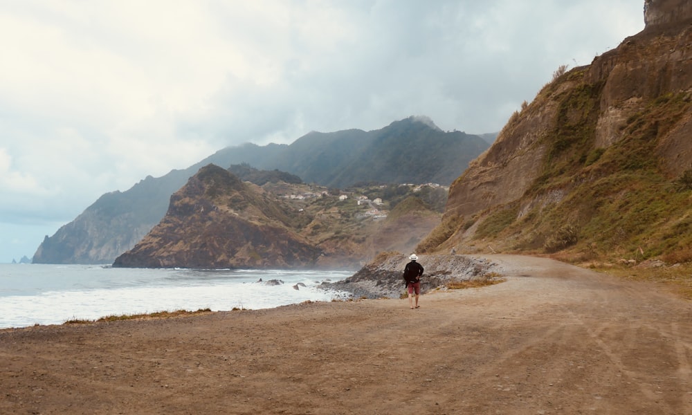 a person walking down a dirt road next to the ocean