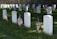Several white gravestones are lined up in rows, each marked with a small American flag on well-maintained green grass. The background features a stone wall. Some of the gravestones are inscribed with the words 'Unknown U.S. Soldier.'