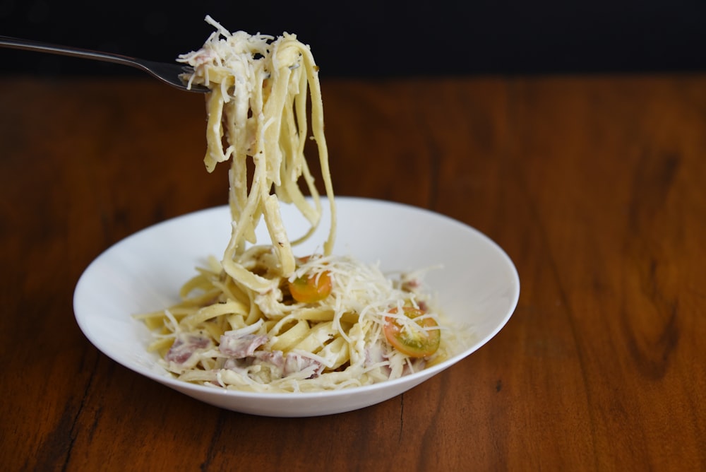 Un tazón blanco lleno de pasta encima de una mesa de madera