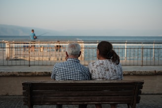 a man and a woman sitting on a bench looking at the ocean