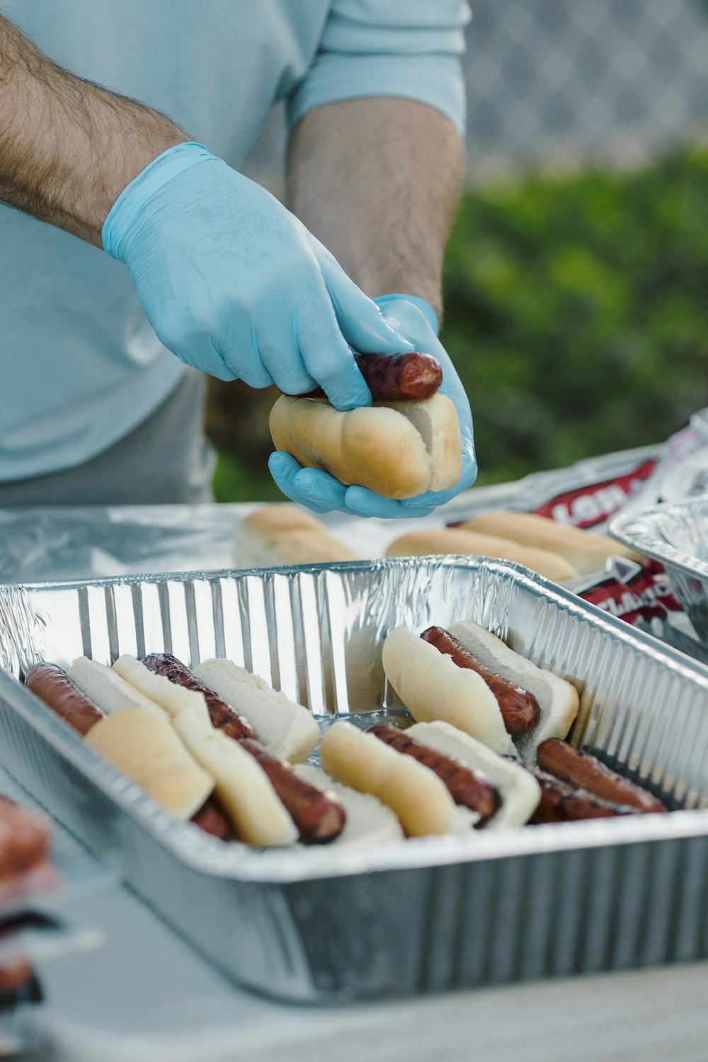 a man in blue gloves is putting hotdogs in a tin