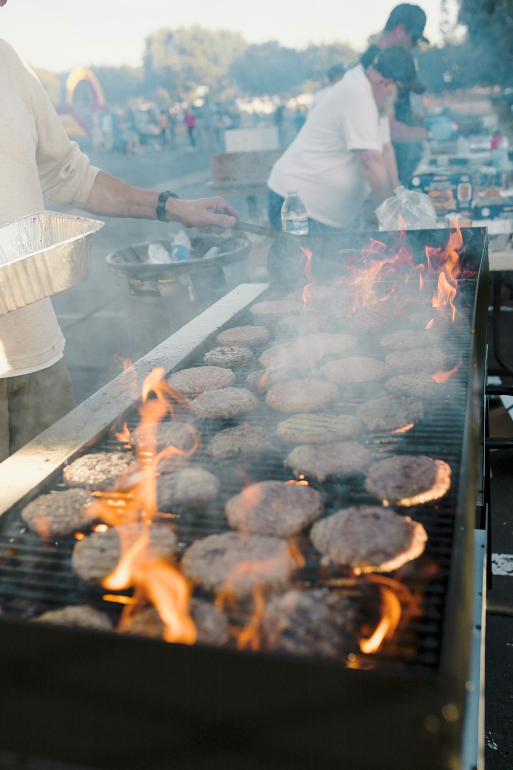 a man cooking hamburgers on a grill with flames