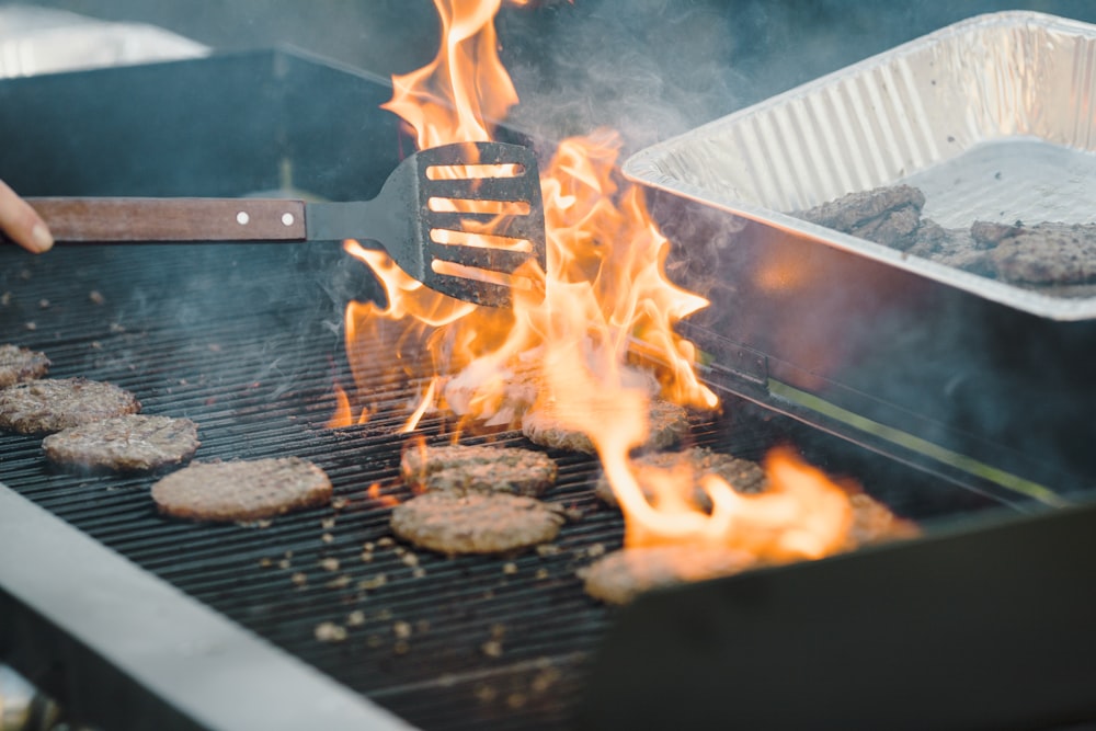 a person grilling hamburgers and hamburger patties on a grill